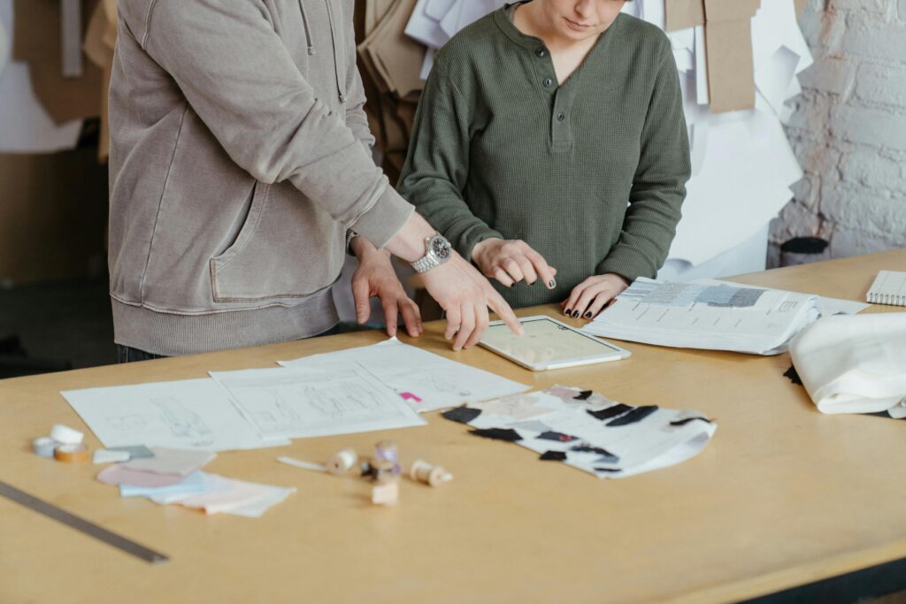 Fashion designers using digital tools and fabric samples in a creative workshop setting.